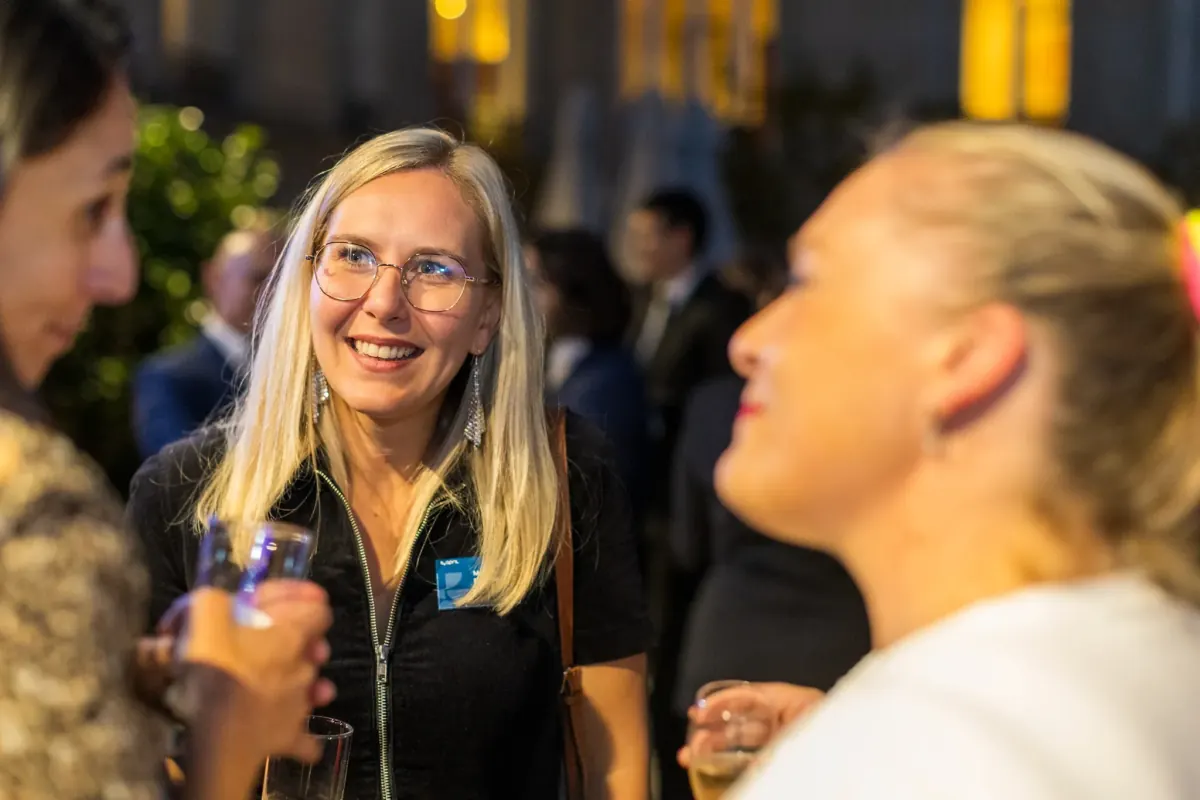Participante souriante en conversation lors d'une soirée d'entreprise, moment à chaud capté pour une diffusion dès le lendemain
