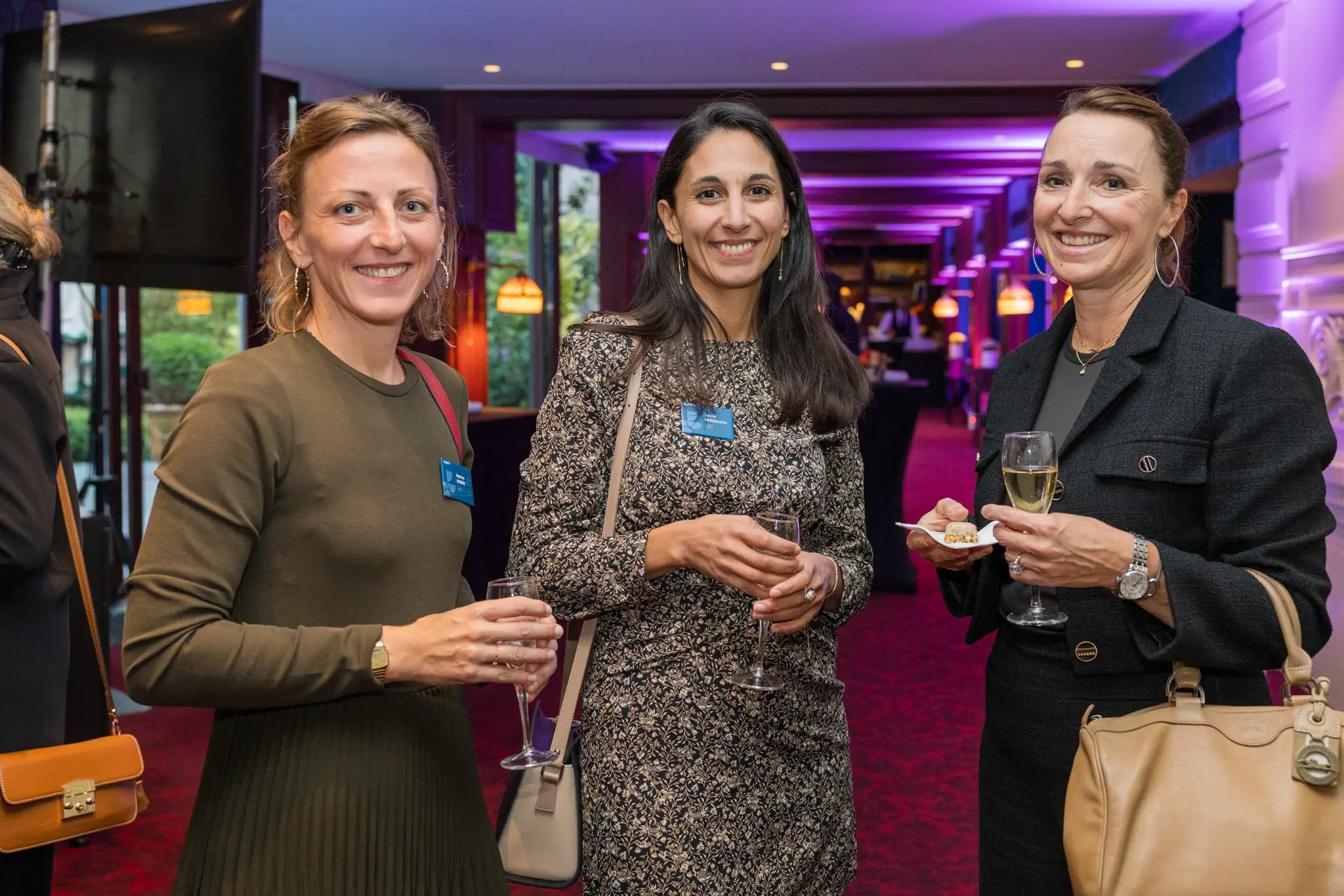 Trois participantes verre à la main lors d'un cocktail d'entreprise, mains occupées et postures détendues, exemple de pose naturelle en événement