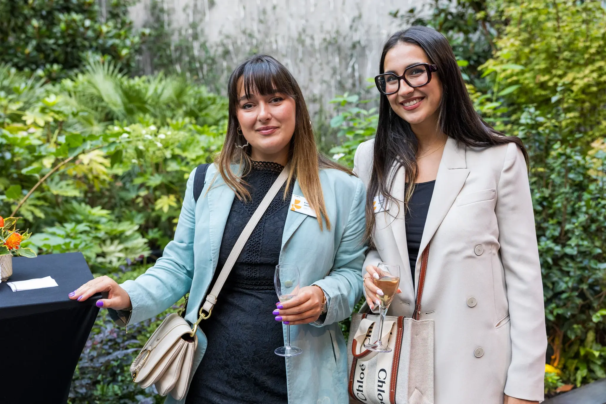 Deux invitées verre à la main lors d'un cocktail d'entreprise, coudes légèrement ouverts, exemple de pose féminine naturelle en événement