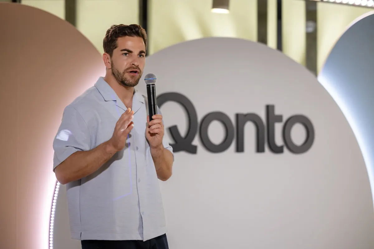 Intervenant au micro devant le logo de son entreprise lors d'une prise de parole